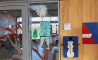 An der Glastür und der Wand zu einem Klassenzimmer der Grundschule Infanteriestraße hängen drei gemalte Bilder von Weihnachtsbäumen, ein Papierstern und jeweils ein Schneemann und ein Nikolaus aus aufgeklebten buntem Papier.apier 