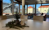 Ausschnitt der Mensa der Grundschule Infanteriestraße mit Tischen und Stühlen. auf den Tischen und an den Säulen ist Weihnachtsdekoration. Auf den Tischen sind Tannenzweige und an den Säulen Papierweihnachtsbäume.