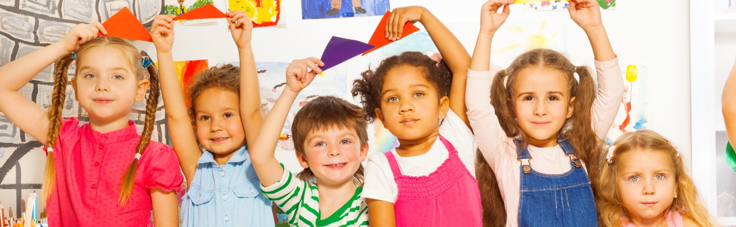 Header: Mehrere Kinder haben zusammen gebastelt. Jetzt hält jeder von ihnen ein buntes Papier hoch. 