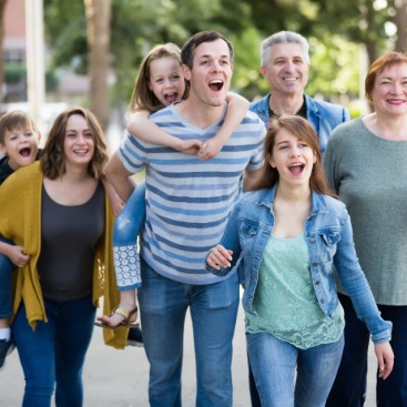 Kachel: Eine Familie mit drei Kindern, Eltern und Großeltern sind gemeinsam draußen unterwegs. 