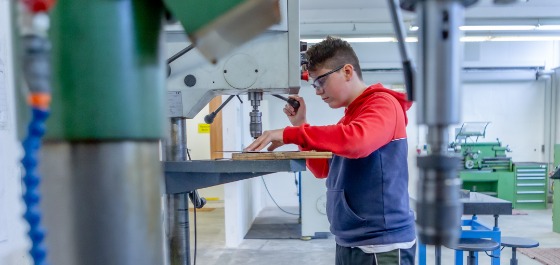 Titelbild: Jugendlicher Schüler bohrt in einer Werkstatt an einer Standbohrmaschine ein Metallstück