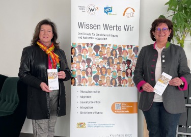 Petra Loibl (MdL) und W³ Projektleiterin am Standort Landshut Gudrun Zollner stehen links und rechts vor einem Rollup, welches das W³ Projekt der gfi beschreibt.