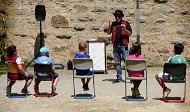 News- Bild: Fünf Kinder sitzen auf Stühlen und schauen einem Mann zu